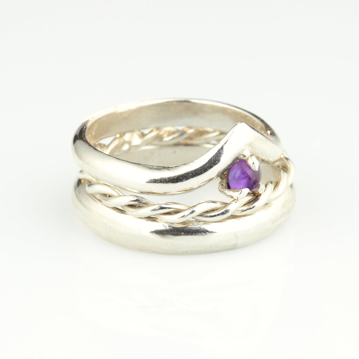 Handgefertigtes Ehering-Set aus 925 Silber auf Leder. 3-teiliges Damen-Set bestehend aus einem 3mm Wishbone-Ring mit Amethyst und einem 2mm Kordelring. Daneben ein massiver 4mm Herrenring im Halbrund-Profil. Zeitloses Design mit lila Edelstein für die Hochzeit. SEO-Keywords: Wishbone Eheringe Silber, Amethyst Trauringe Set, handgefertigte Silberringe, 925 Sterlingsilber Schmuck, Kordelring Hochzeit. Sichtbare Details der hochwertigen Handarbeit und Steinbesetzung.
