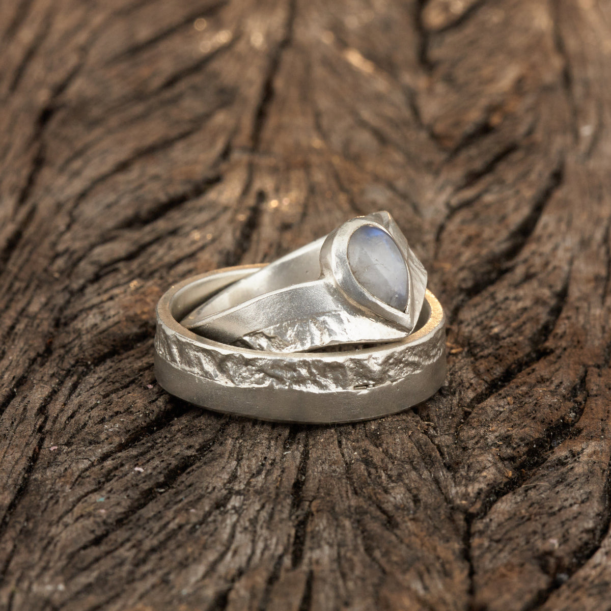 Hochwertiges Eheringe Set aus massivem 925 Sterling Silber mit kontrastreicher Oberfläche halb matt und halb retikuliert. Der Damenring in eleganter Wishbone V-Form trägt einen handgefassten Regenbogen-Mondstein im Tropfenschliff 9x6 mm mit blauem Schimmer. Der Herrenring ist 6x2 mm breit und spiegelt das maritime nordische Design wider. Handgefertigte Markenware aus der Goldschmiede Silberschweif für Paare die exklusiven Edelsteinschmuck und archaische Strukturen suchen