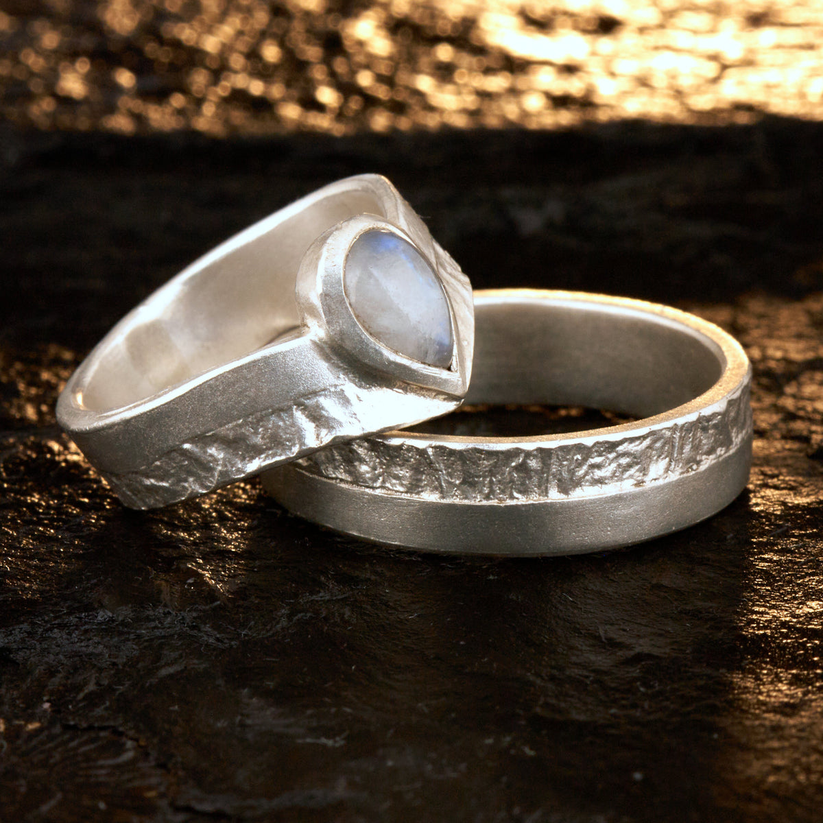 Hochwertiges Eheringe Set aus massivem 925 Sterling Silber mit kontrastreicher Oberfläche halb matt und halb retikuliert. Der Damenring in eleganter Wishbone V-Form trägt einen handgefassten Regenbogen-Mondstein im Tropfenschliff 9x6 mm mit blauem Schimmer. Der Herrenring ist 6x2 mm breit und spiegelt das maritime nordische Design wider. Handgefertigte Markenware aus der Goldschmiede Silberschweif für Paare die exklusiven Edelsteinschmuck und archaische Strukturen suchen