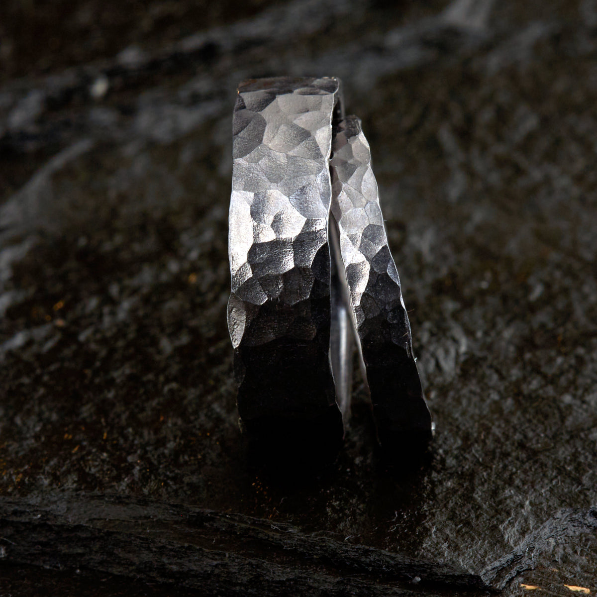 Handgefertigtes Ehering-Set aus massivem Tantal auf rustikalem Leder. Herrenring (6mm) und Damenring (4mm) mit markanter, gehämmerter Oberfläche in dunklem Anthrazit. Einzigartige Schmiedekunst für exklusive Hochzeitsringe. SEO-Keywords: Tantal Eheringe gehämmert, dunkle Trauringe, Tantalum Wedding Bands, nachhaltiger Luxusschmuck, seltene Edelmetalle Hochzeit. Sichtbare Details der individuellen Textur und des tiefen, metallischen Glanzes.