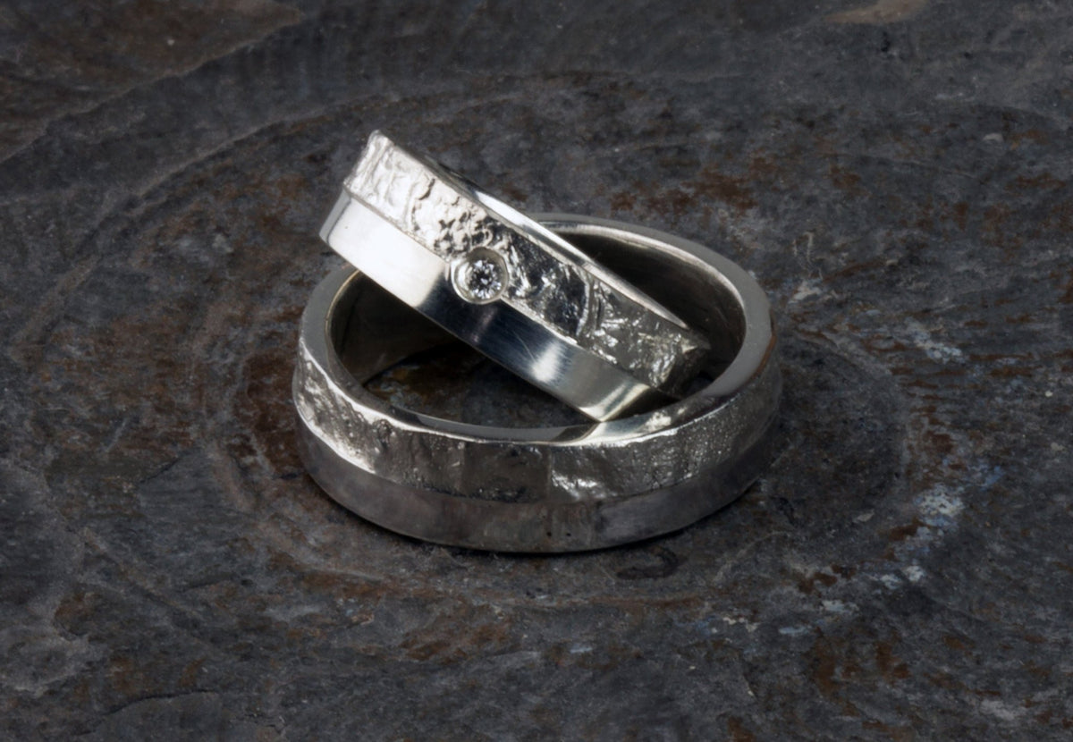 Massive Trauringe aus 925 Silber handgefertigt. Eheringe mit markanter Schieferstruktur im Kontrast zu mattierten Oberflächen. Damenring ca. 6mm breit mit einem bündig gefassten 2mm Brillanten (TW/si). Herrenring ca. 6mm breit, massiv und charakterstark. Einzigartiges Partnerring-Set mit organischer Textur, inspiriert von natürlichem Fels. Handgemacht in eigener Werkstatt in Deutschland, keine CNC-Massenware. Hochwertige Unikate für Individualisten