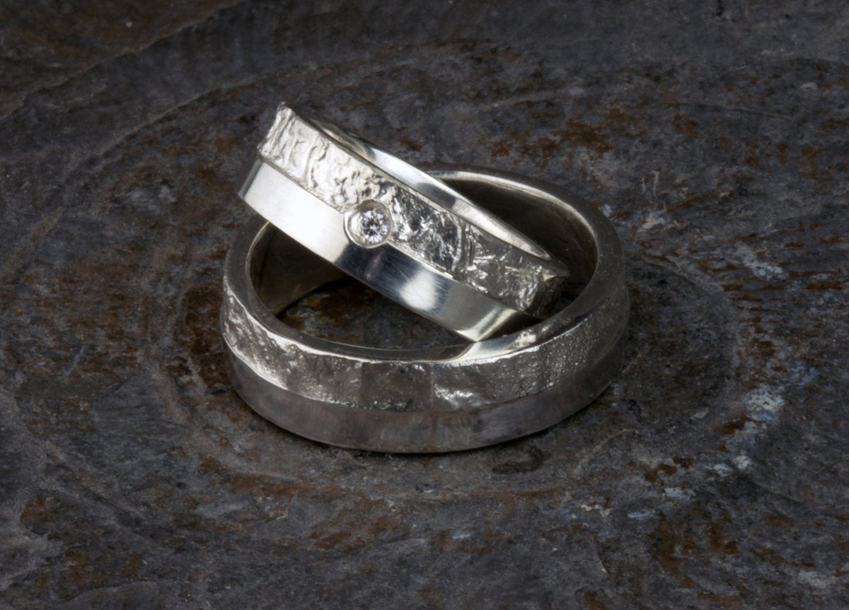 Massive Trauringe aus 925 Silber handgefertigt. Eheringe mit markanter Schieferstruktur retikuliert im Kontrast zu mattierten Oberflächen. Damenring ca. 6mm breit mit einem bündig gefassten 2mm Brillanten (TW/si). Herrenring ca. 6mm breit, massiv und charakterstark. Einzigartiges Partnerring-Set mit organischer Textur, inspiriert von natürlichem Fels. Handgemacht in eigener Werkstatt in Deutschland, keine CNC-Massenware. Hochwertige Unikate für Individualisten